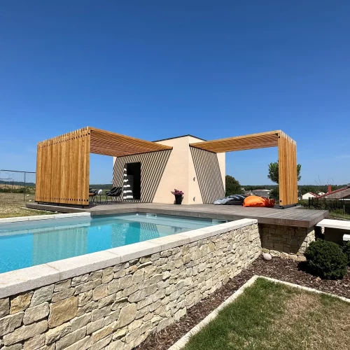 En premier plan, la piscine habillée de pierres de Bourgogne. Derrière l'abri de jardin avec les deux pergolas ainsi que la terrasse.